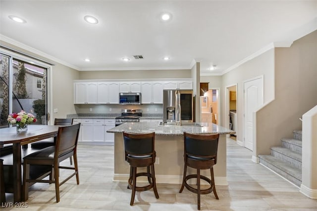 kitchen featuring light stone countertops, white cabinets, stainless steel appliances, and a kitchen island with sink