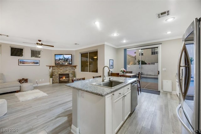 kitchen featuring white cabinetry, stainless steel appliances, a kitchen island with sink, light wood-type flooring, and sink