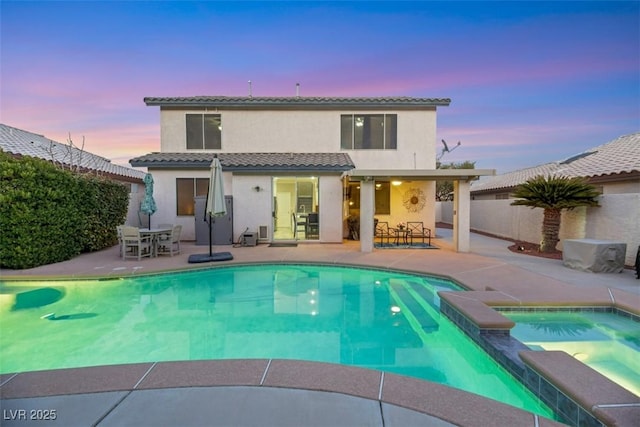 back house at dusk with a pool with hot tub and a patio