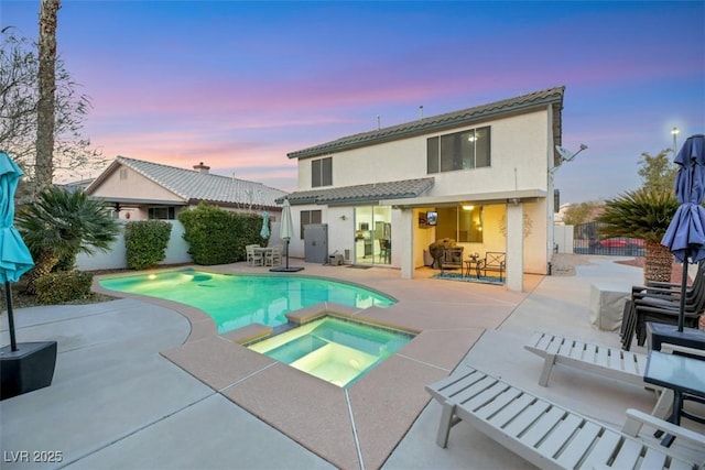 back house at dusk with a pool with hot tub and a patio area