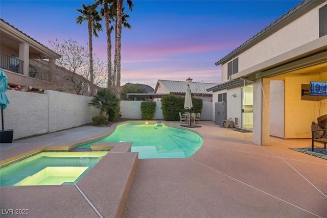 pool at dusk with an in ground hot tub and a patio