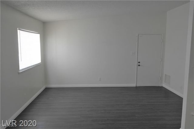 spare room featuring a textured ceiling and dark hardwood / wood-style floors