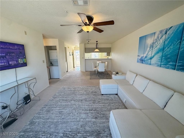 living room featuring ceiling fan, light colored carpet, and a textured ceiling