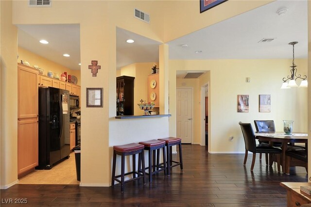 kitchen with black appliances, light brown cabinets, a kitchen breakfast bar, hanging light fixtures, and dark hardwood / wood-style floors