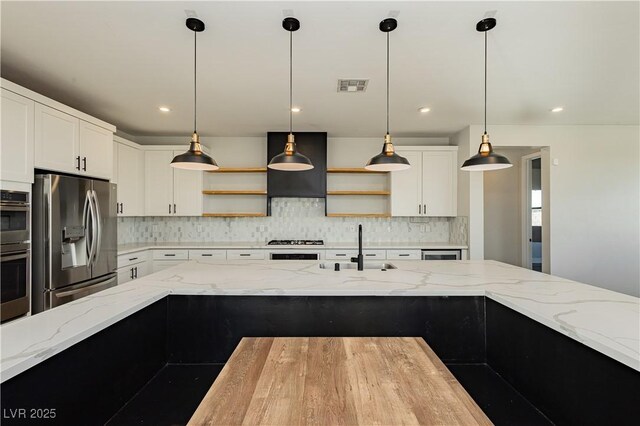 kitchen with light stone counters, appliances with stainless steel finishes, hanging light fixtures, and white cabinets