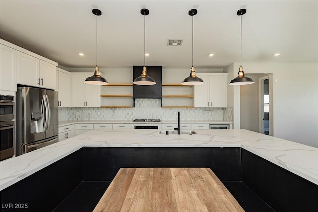 kitchen with pendant lighting, light stone countertops, stainless steel appliances, and white cabinets