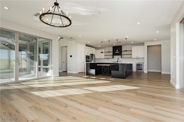 kitchen featuring sink, hanging light fixtures, a center island with sink, white cabinets, and backsplash