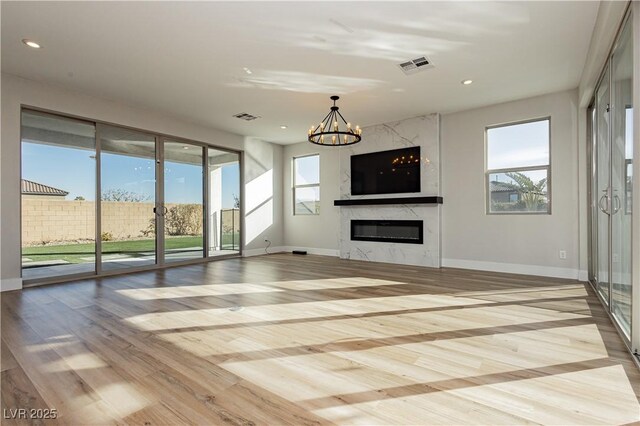 unfurnished living room with a premium fireplace, a notable chandelier, and light wood-type flooring