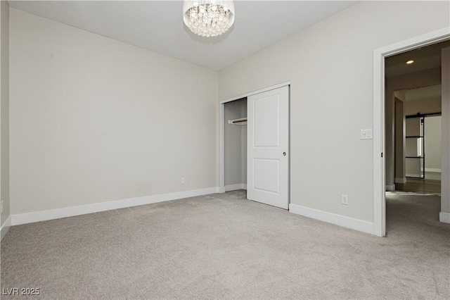 unfurnished bedroom with a closet, light colored carpet, a barn door, and a chandelier