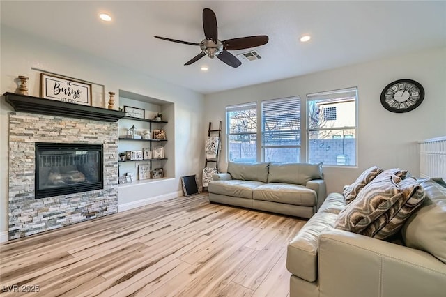 living room with ceiling fan, built in shelves, a fireplace, and light hardwood / wood-style floors