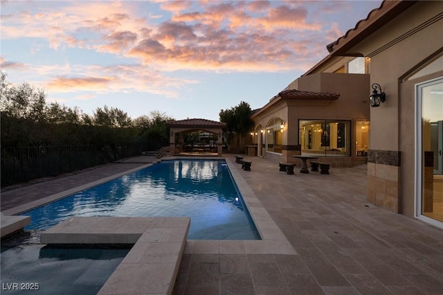 pool at dusk with a gazebo and a patio area