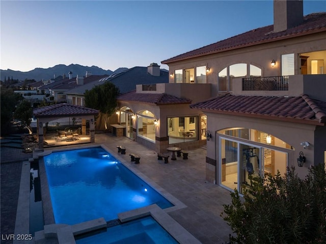 pool at dusk featuring a gazebo, area for grilling, a mountain view, an in ground hot tub, and a patio