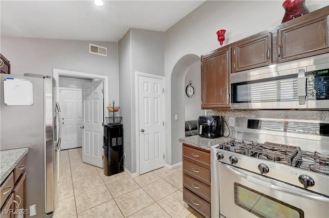 kitchen featuring light stone countertops, appliances with stainless steel finishes, lofted ceiling, backsplash, and light tile patterned floors