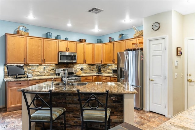 kitchen featuring appliances with stainless steel finishes, sink, a breakfast bar, a center island with sink, and stone counters