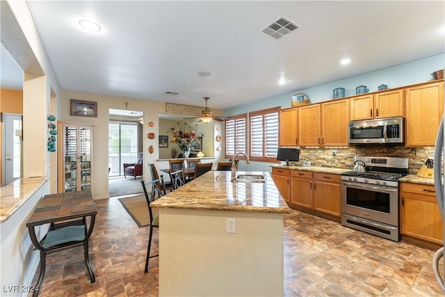 kitchen featuring a center island with sink, a kitchen bar, sink, light stone countertops, and stainless steel appliances