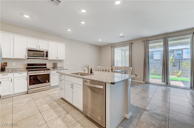 kitchen featuring light stone countertops, appliances with stainless steel finishes, white cabinetry, sink, and a center island with sink