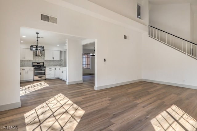 unfurnished living room with a high ceiling, an inviting chandelier, and dark hardwood / wood-style floors