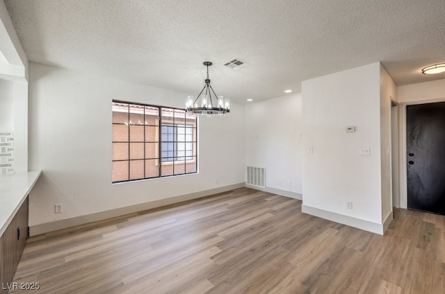 unfurnished dining area featuring hardwood / wood-style floors, a textured ceiling, and a notable chandelier