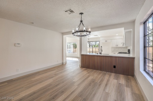 kitchen featuring kitchen peninsula, decorative backsplash, sink, white cabinetry, and a chandelier