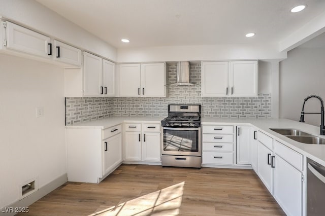 kitchen with appliances with stainless steel finishes, backsplash, wall chimney range hood, white cabinets, and sink