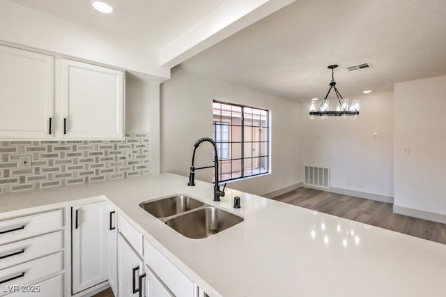 kitchen with kitchen peninsula, a notable chandelier, sink, and white cabinetry