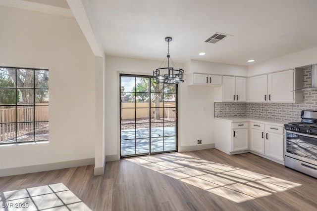 kitchen featuring white cabinetry, stainless steel gas range oven, backsplash, a notable chandelier, and light wood-type flooring