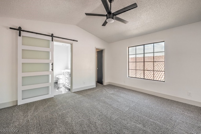 unfurnished bedroom featuring ceiling fan, a textured ceiling, ensuite bath, and a barn door