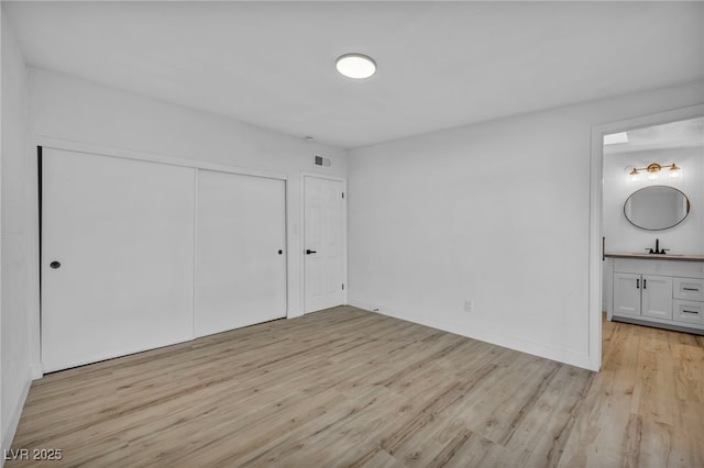 unfurnished bedroom featuring a closet, light hardwood / wood-style floors, connected bathroom, and sink