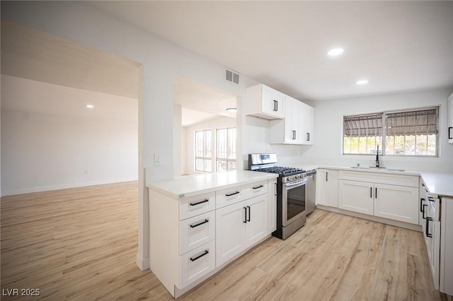 kitchen with sink, gas range, white cabinetry, and light hardwood / wood-style floors