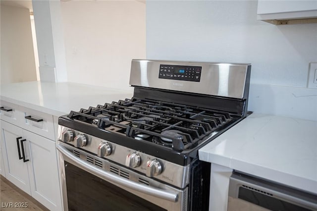 room details with light wood-type flooring, stainless steel gas stove, white cabinets, and dishwashing machine