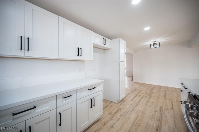 kitchen with light wood-type flooring, white cabinets, light stone counters, and oven