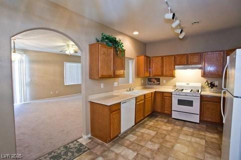 kitchen featuring white appliances, rail lighting, light carpet, sink, and ceiling fan