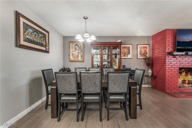 dining space featuring a notable chandelier, a textured ceiling, and a brick fireplace