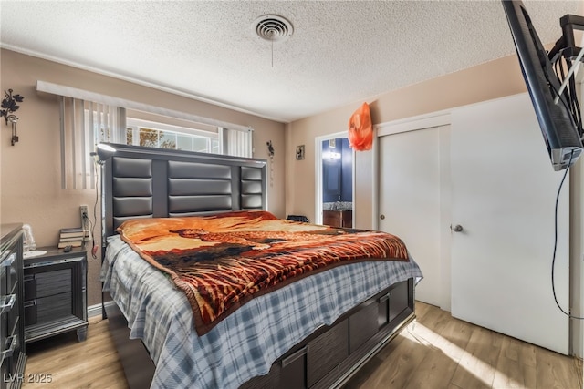 bedroom with hardwood / wood-style flooring, ensuite bath, a textured ceiling, and a closet