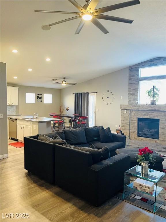 living room featuring lofted ceiling, a fireplace, sink, and light hardwood / wood-style flooring