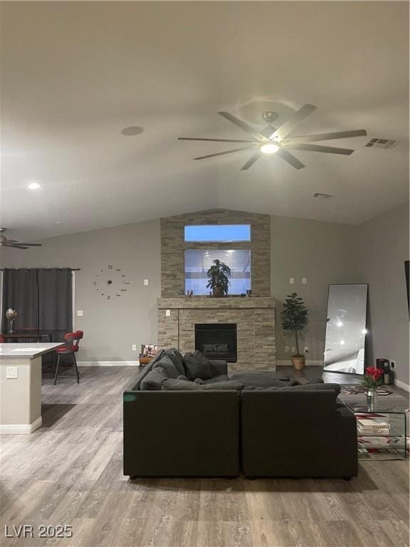 living room with vaulted ceiling, a tiled fireplace, and wood-type flooring