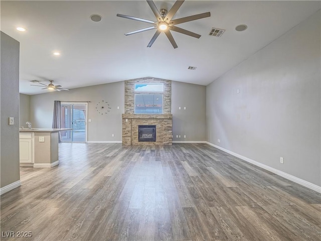 unfurnished living room featuring a ceiling fan, visible vents, lofted ceiling, a stone fireplace, and light wood-type flooring