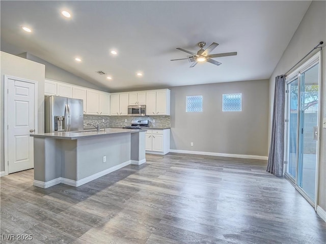 kitchen with stainless steel appliances, light wood-style floors, decorative backsplash, and vaulted ceiling