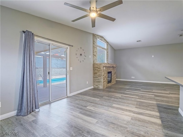 unfurnished living room featuring a glass covered fireplace, wood finished floors, a healthy amount of sunlight, and baseboards