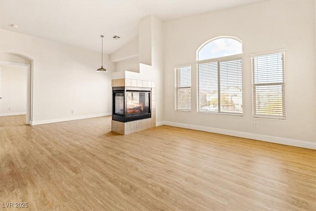 unfurnished living room featuring lofted ceiling, light hardwood / wood-style flooring, and a tiled fireplace