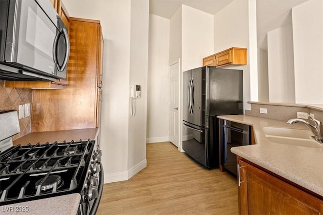 kitchen with sink, light hardwood / wood-style floors, backsplash, and black appliances