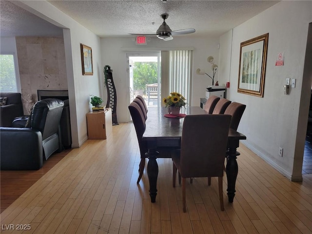 dining space with light hardwood / wood-style floors, a textured ceiling, a tile fireplace, and ceiling fan