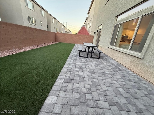 patio terrace at dusk featuring a lawn