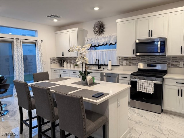 kitchen with a kitchen bar, white cabinetry, appliances with stainless steel finishes, and decorative backsplash