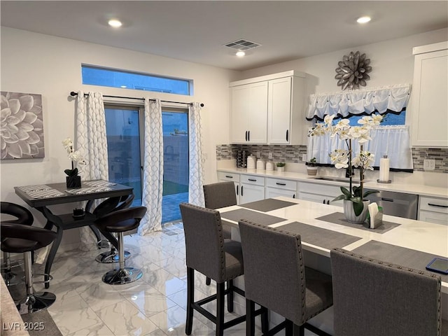 kitchen featuring tasteful backsplash, stainless steel dishwasher, sink, a kitchen breakfast bar, and white cabinets