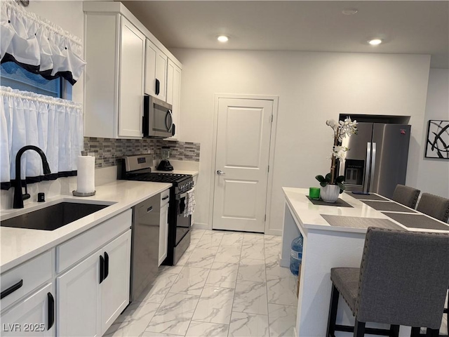 kitchen with white cabinetry, stainless steel appliances, backsplash, a breakfast bar, and sink