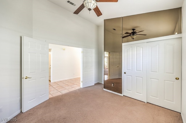 unfurnished bedroom with light carpet, a closet, a towering ceiling, and ceiling fan