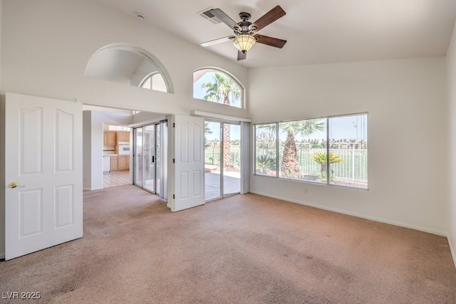 carpeted spare room with ceiling fan, a healthy amount of sunlight, and high vaulted ceiling