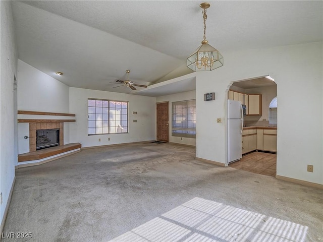 unfurnished living room with ceiling fan with notable chandelier, a tile fireplace, light carpet, and vaulted ceiling