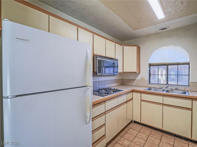 kitchen featuring light tile patterned floors, tile countertops, stainless steel gas cooktop, white refrigerator, and sink